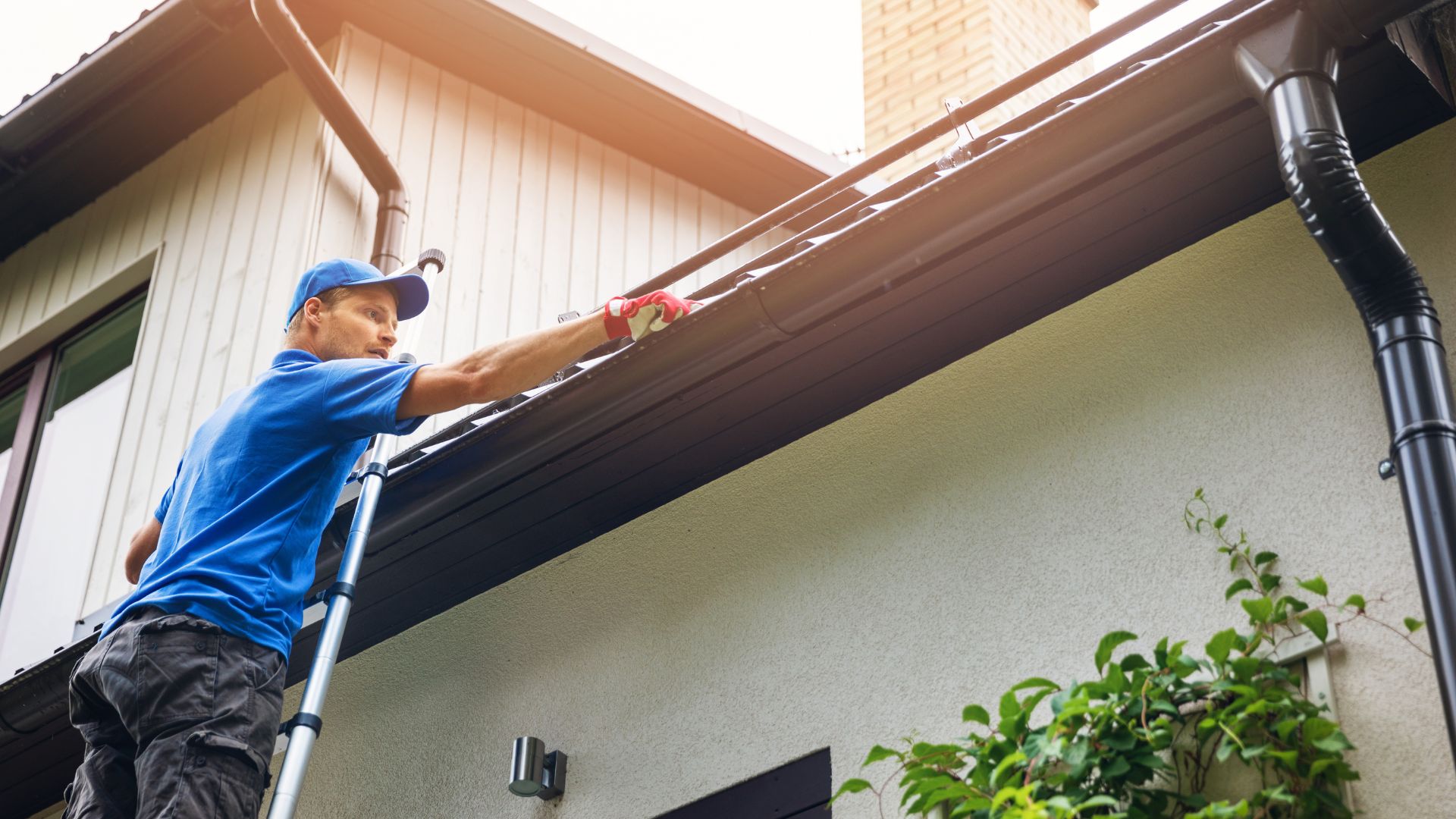 Worker cleaning gutters on a house using a ladder and cleaning cloth