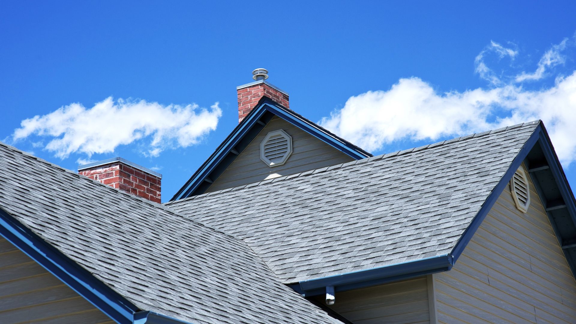 Gray shingled roof with brick chimneys against bright blue sky