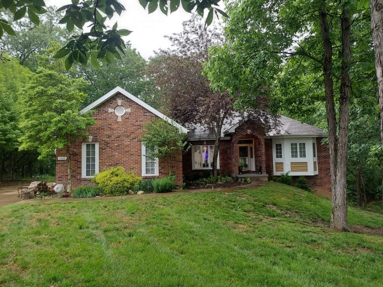 Brick ranch house with landscaped yard surrounded by green trees