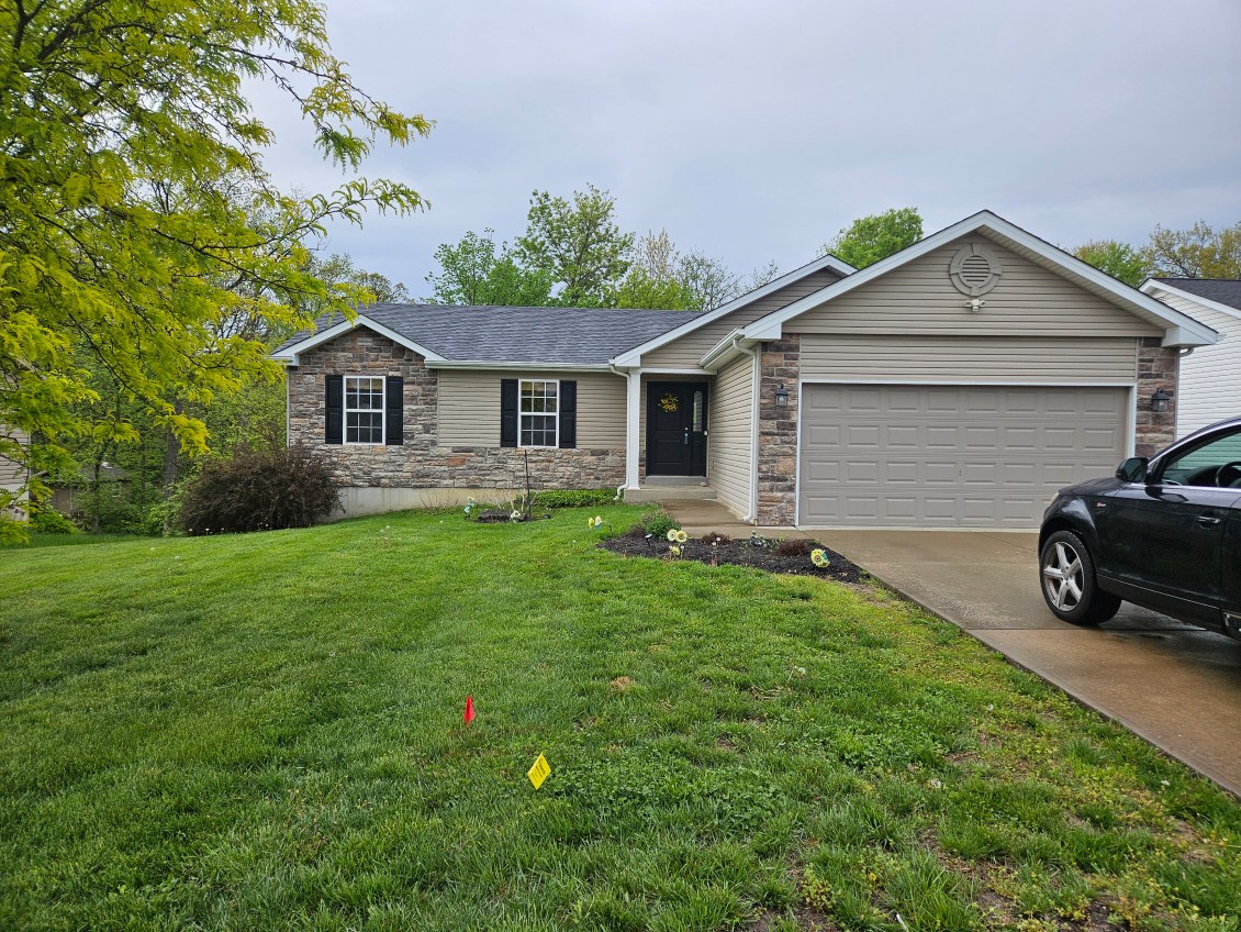 Ranch-style house with stone accents, green lawn, and black SUV in driveway