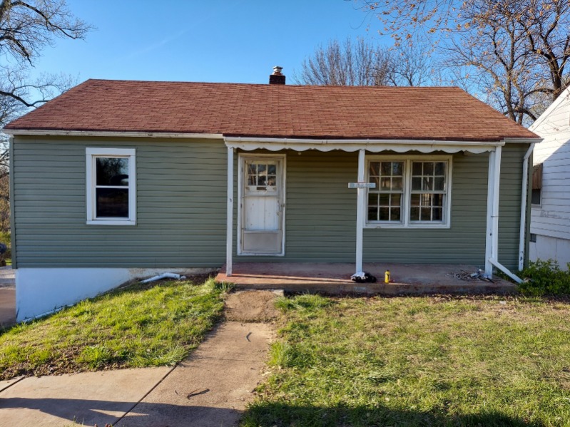 Small green single-story house with brown roof and white trim on sunny day
